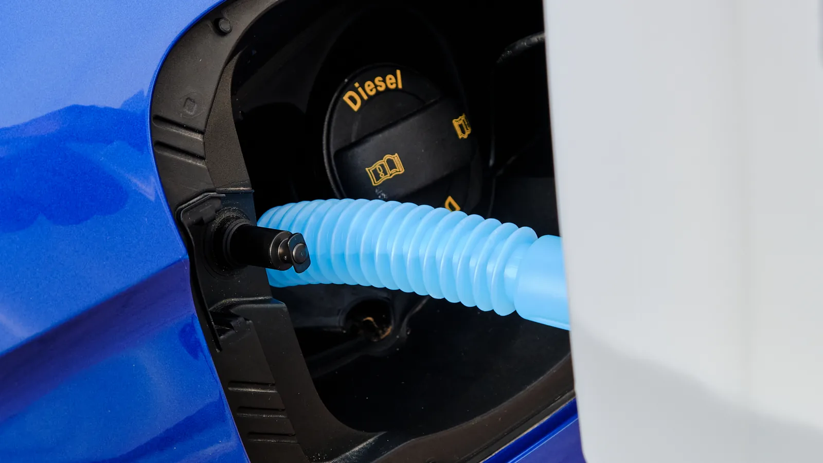 Niebieski wężyk z kanistra we wlewie AdBlue obok korka z napisem Diesel