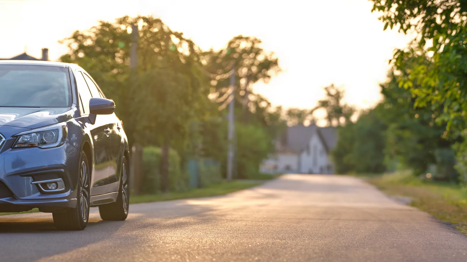 Granatowe auto przy poboczu podmiejskiej drogi w ciepłym świetle zachodzącego słońca