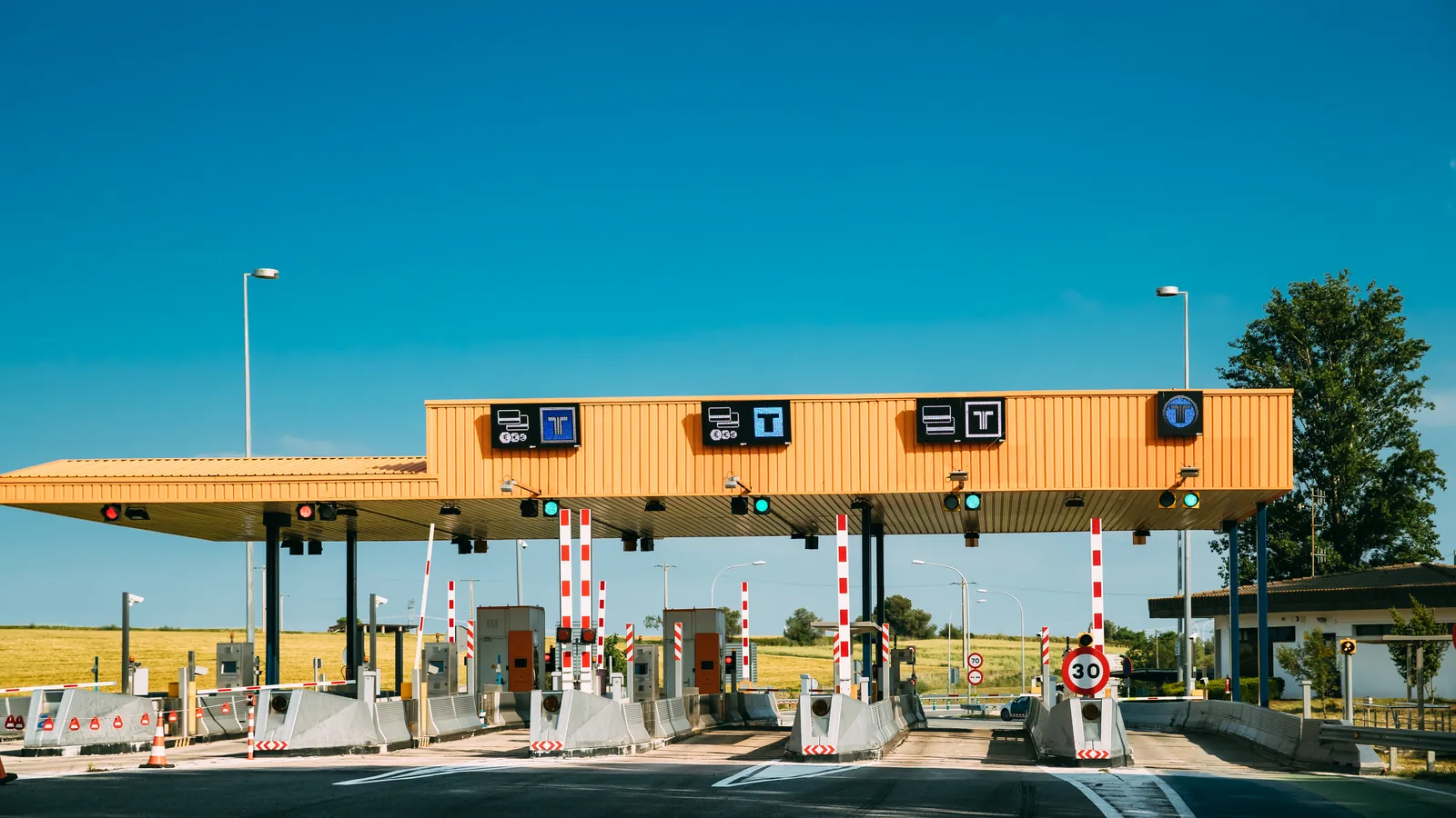 Punkt poboru opłat z żółtym zadaszeniem, szlabanami i ograniczeniem do 30 kilometrów