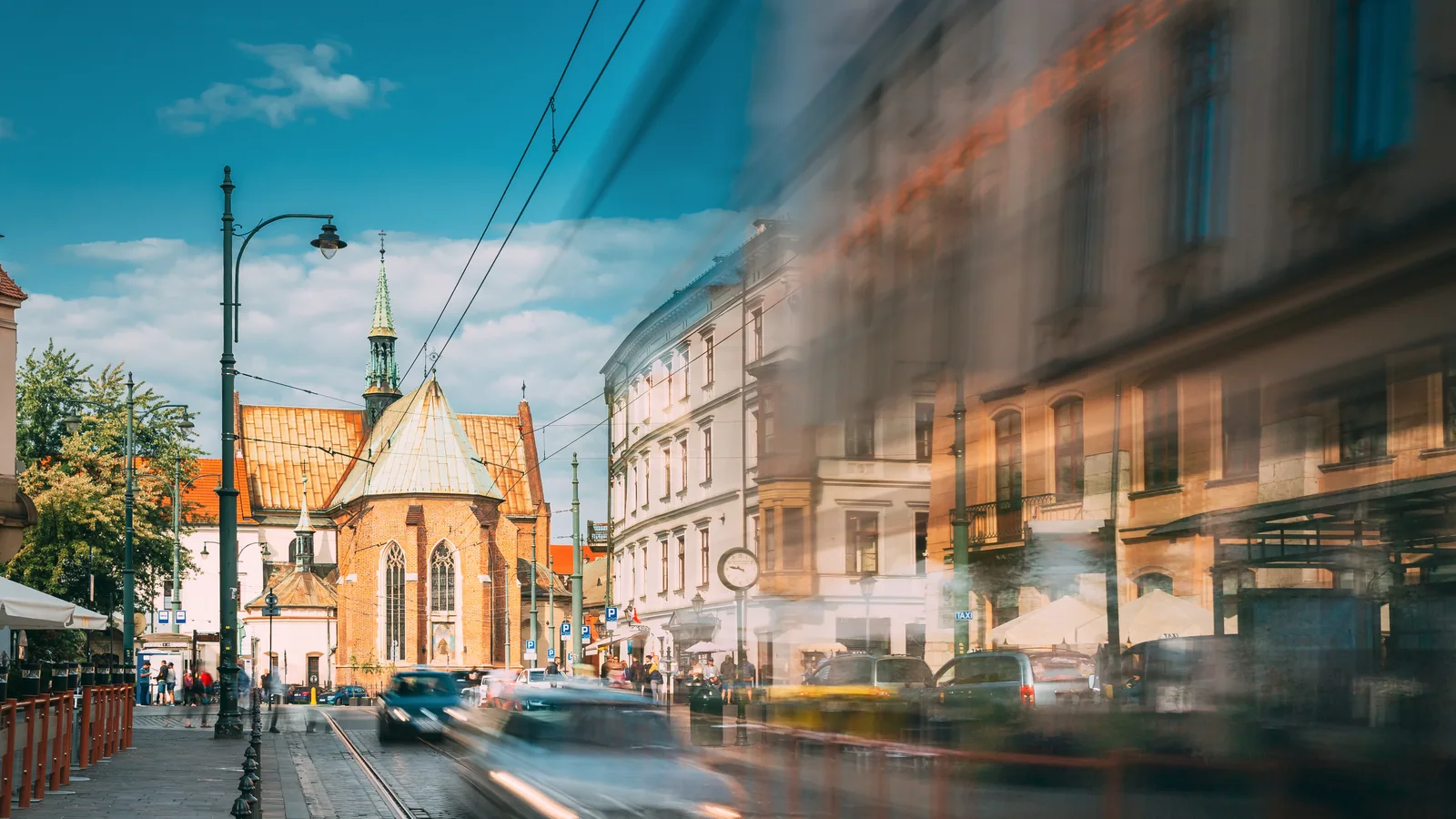 Rozmyte w ruchu auta i tramwaj na ulicy starego miasta, w tle ceglany kościół i kamienice