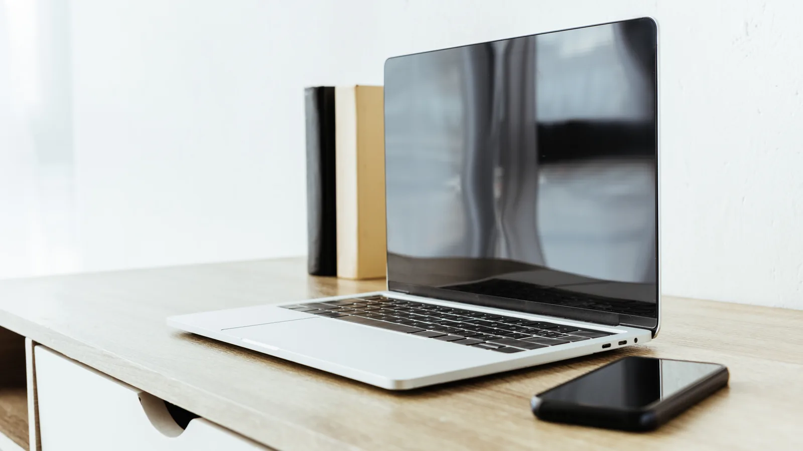 Otwarty laptop z wygaszonym ekranem i telefon na jasnym drewnianym blacie